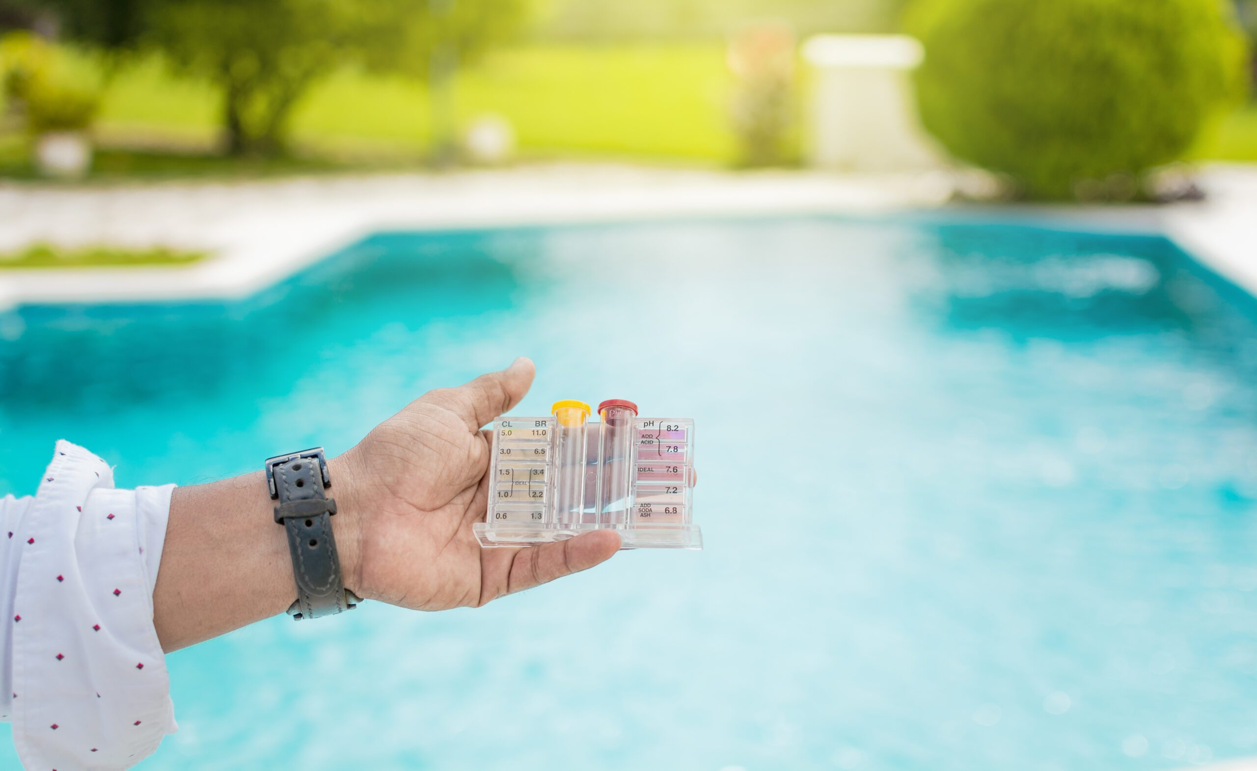 Hand holding Water Test Kit on blurred pool background, Hand holding a pool ph and chlorine tester, Person holding complete water test kit with blurred pool background